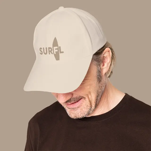 A man wearing a natural tan SURFL cap embroidered with the surfboard-through-the-F logo over a chocolate brown tee